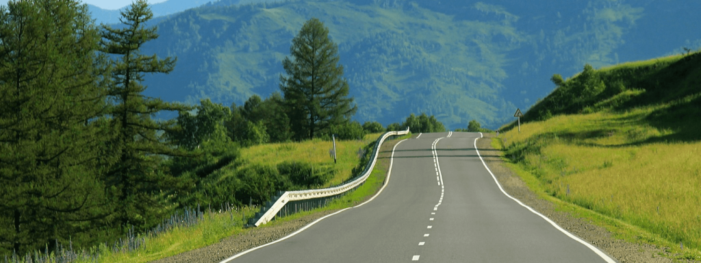 An uneven windy road surrounded by green foliage and mountains