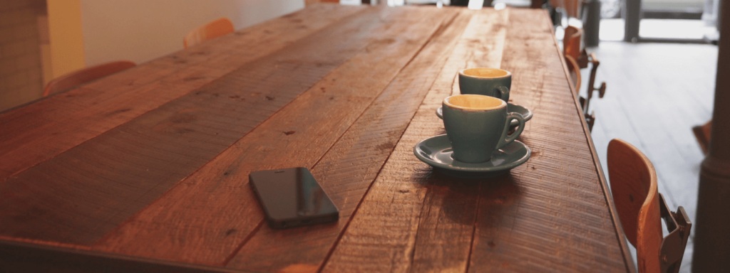 Two coffee cups and an iPhone on a wooden table